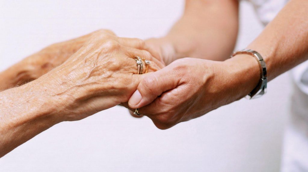 Persona sosteniendo las manos de un adulto mayor